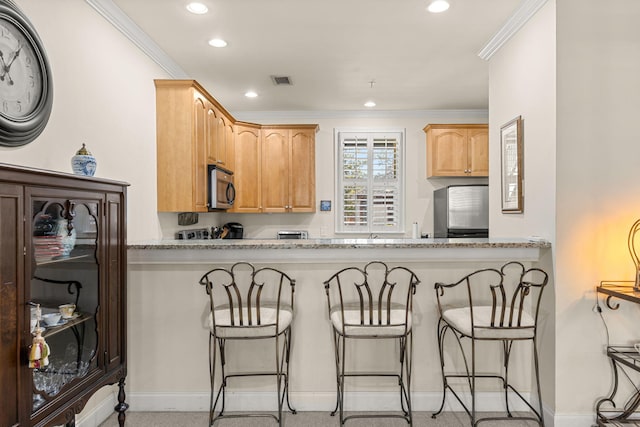 kitchen with stainless steel microwave, fridge, ornamental molding, recessed lighting, and a breakfast bar