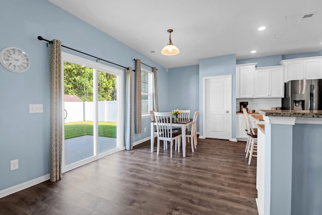 kitchen with stainless steel fridge, dark hardwood / wood-style flooring, dark stone counters, white cabinets, and hanging light fixtures