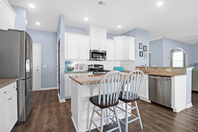 kitchen featuring a kitchen bar, white cabinetry, dark wood-type flooring, and stainless steel appliances