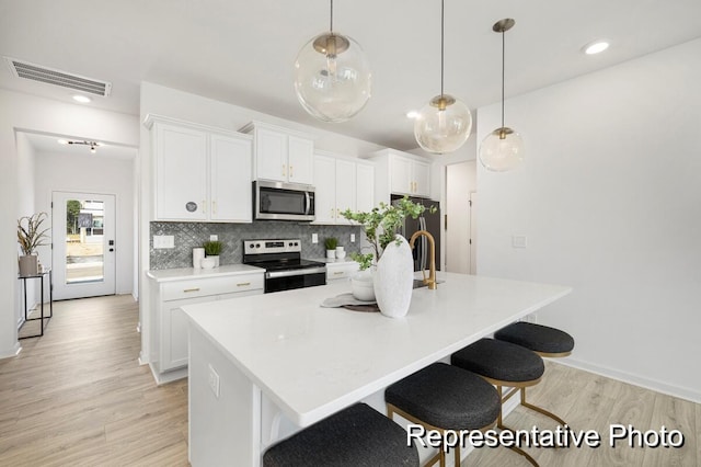 kitchen featuring a breakfast bar, a kitchen island with sink, stainless steel appliances, white cabinets, and decorative light fixtures