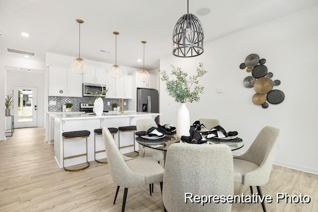 dining space featuring sink, light hardwood / wood-style floors, and a notable chandelier