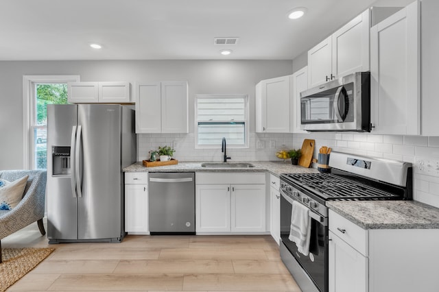 kitchen with appliances with stainless steel finishes, white cabinetry, sink, and light hardwood / wood-style floors