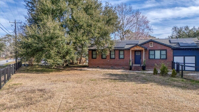 view of front of home featuring brick siding, solar panels, crawl space, fence, and a front lawn