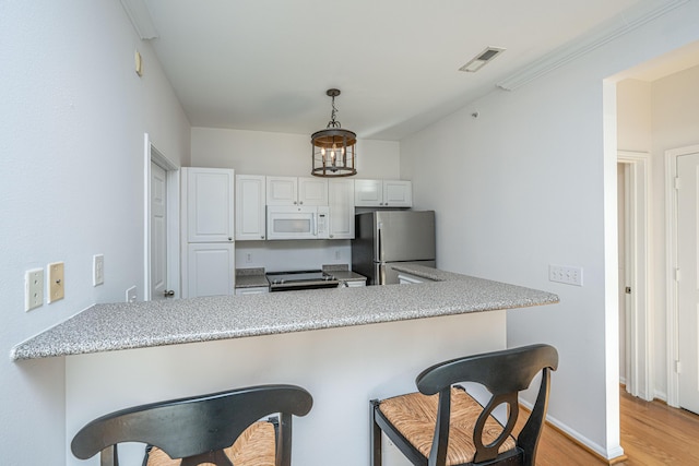 kitchen with white cabinetry, kitchen peninsula, stainless steel fridge, a breakfast bar area, and hanging light fixtures