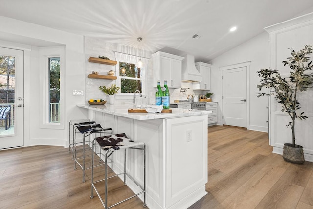 kitchen featuring custom range hood, white cabinets, a kitchen bar, kitchen peninsula, and light wood-type flooring