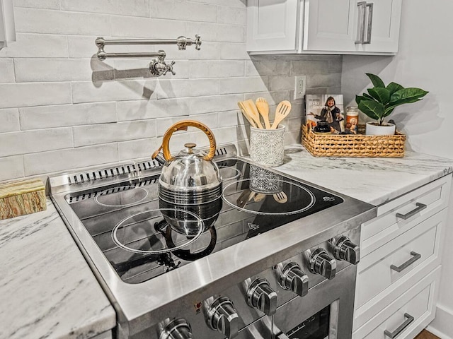 interior details featuring light stone counters, stainless steel electric stove, decorative backsplash, and white cabinets