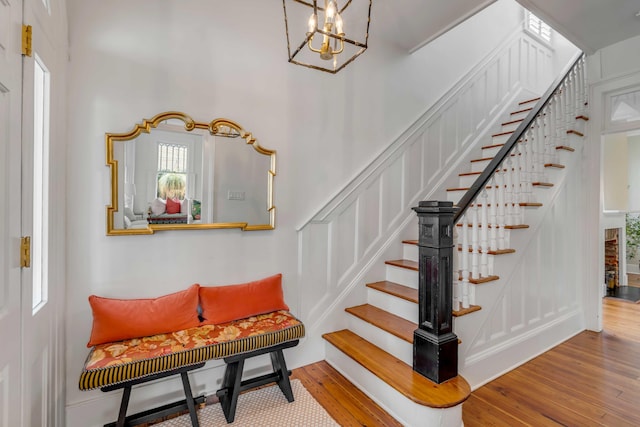 staircase featuring wood finished floors and an inviting chandelier