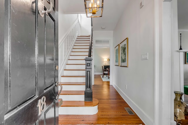 foyer entrance with a notable chandelier, visible vents, stairway, hardwood / wood-style floors, and baseboards