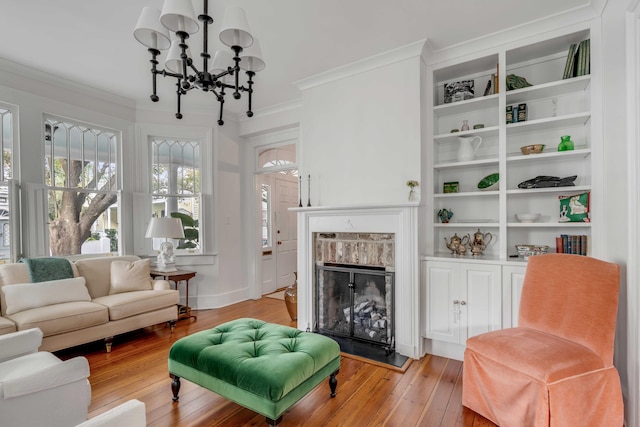 living room with a chandelier, a fireplace with raised hearth, crown molding, and light wood-style flooring