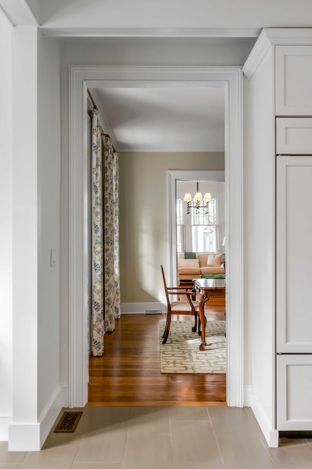 hall featuring an inviting chandelier, tile patterned flooring, visible vents, and baseboards