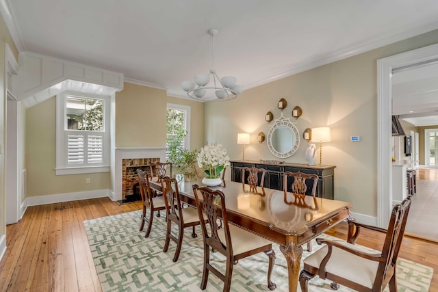 dining space featuring ornamental molding, a brick fireplace, light wood finished floors, and an inviting chandelier