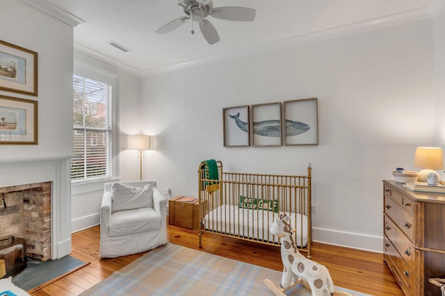 bedroom with a fireplace, crown molding, visible vents, hardwood / wood-style floors, and baseboards