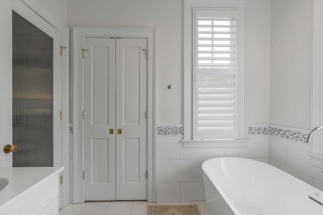 bathroom with a soaking tub, a wainscoted wall, tile patterned flooring, vanity, and tile walls