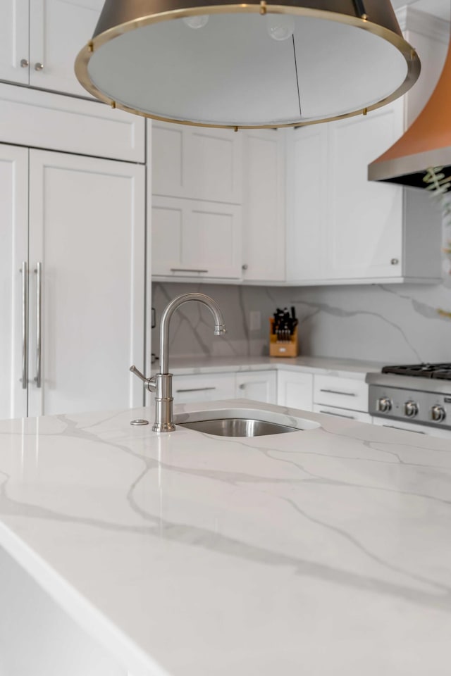 kitchen featuring light stone counters, stove, a sink, white cabinetry, and wall chimney range hood