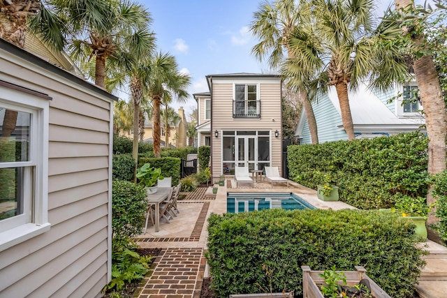 back of property featuring a patio, a balcony, and an outdoor pool