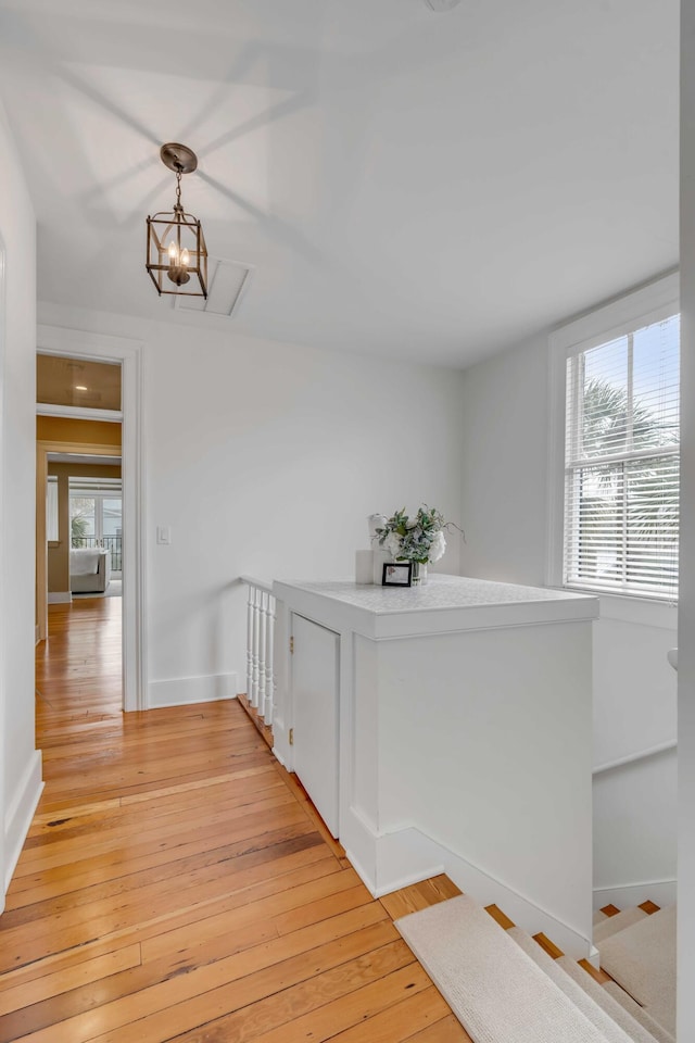 hallway with light wood finished floors, an inviting chandelier, an upstairs landing, and baseboards