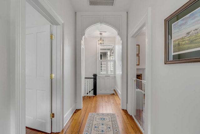 hall with light wood-style floors, visible vents, and an upstairs landing