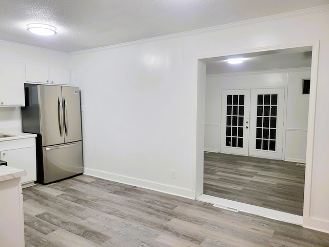 kitchen featuring a textured ceiling, white cabinetry, french doors, stainless steel refrigerator, and light wood-type flooring