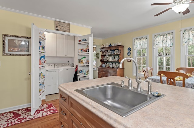 kitchen with sink, light wood-type flooring, washer and clothes dryer, ceiling fan, and ornamental molding