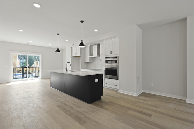 564 Scholar Way, Summerville, SC 29486 - kitchen featuring double oven, white cabinetry, wall chimney exhaust hood, light wood-type flooring, and an island with sink
