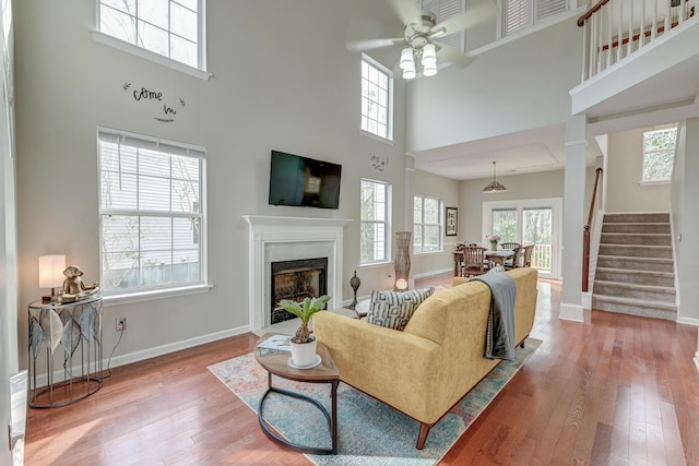 living area featuring baseboards, stairs, a fireplace, hardwood / wood-style flooring, and a ceiling fan