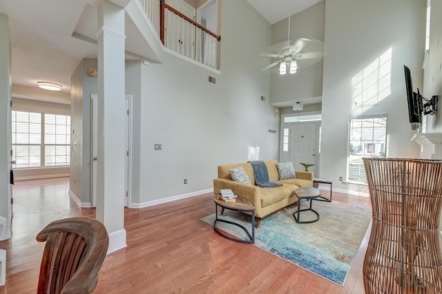 living area with a wealth of natural light, light wood-type flooring, ceiling fan, and decorative columns