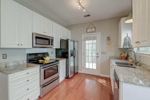 kitchen with baseboards, light wood finished floors, a sink, appliances with stainless steel finishes, and white cabinetry