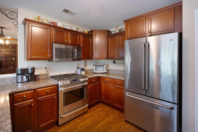 160 Syrr Run Rd, Saint George, SC 29477 - kitchen with stainless steel appliances, wood finished floors, a textured ceiling, light stone counters, and brown cabinetry