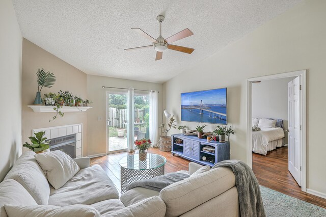 living room featuring a textured ceiling, lofted ceiling, a tiled fireplace, dark hardwood / wood-style flooring, and ceiling fan