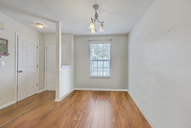 empty room with a textured ceiling, hardwood / wood-style floors, and a notable chandelier