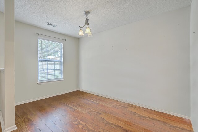 unfurnished room with an inviting chandelier, a textured ceiling, and hardwood / wood-style floors