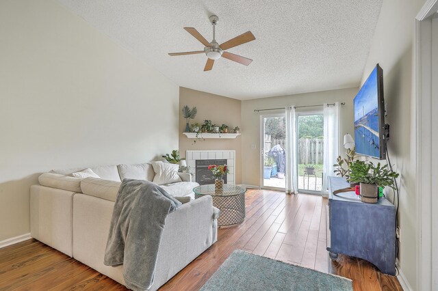 living room featuring a textured ceiling, a tile fireplace, hardwood / wood-style floors, and ceiling fan