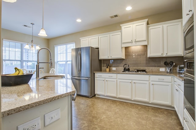 kitchen with appliances with stainless steel finishes, white cabinets, decorative light fixtures, and sink