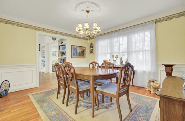 dining space with built in features, a wainscoted wall, a notable chandelier, and ornamental molding