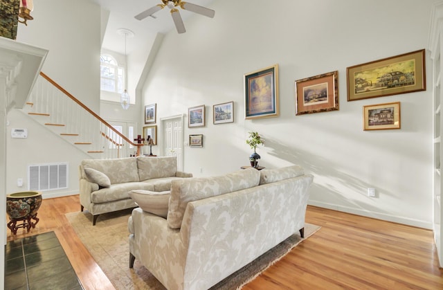 living area with visible vents, stairway, a high ceiling, light wood-style floors, and baseboards