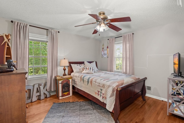 bedroom with hardwood / wood-style flooring, multiple windows, ceiling fan, and a textured ceiling