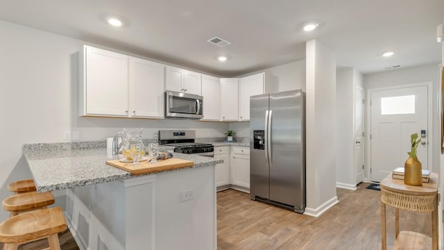 518 Golden Embers Way, Summerville, SC 29486 - kitchen with appliances with stainless steel finishes, a peninsula, light wood-type flooring, white cabinetry, and a kitchen breakfast bar