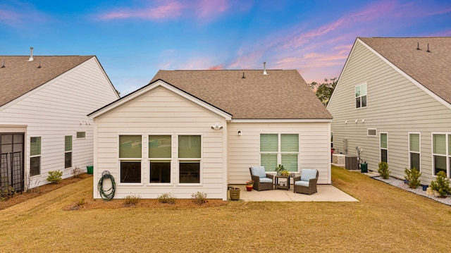back of property at dusk with roof with shingles, central AC unit, an outdoor living space, a yard, and a patio area