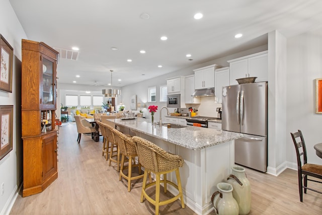 kitchen with a breakfast bar, appliances with stainless steel finishes, under cabinet range hood, a sink, and a large island