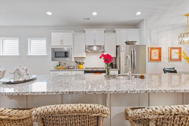 kitchen featuring visible vents, a kitchen bar, stainless steel appliances, under cabinet range hood, and a sink