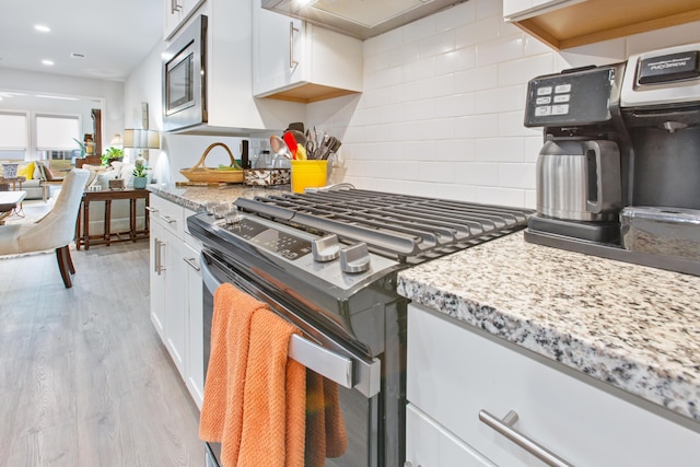 kitchen with wall chimney range hood, white cabinets, appliances with stainless steel finishes, and light wood-style floors