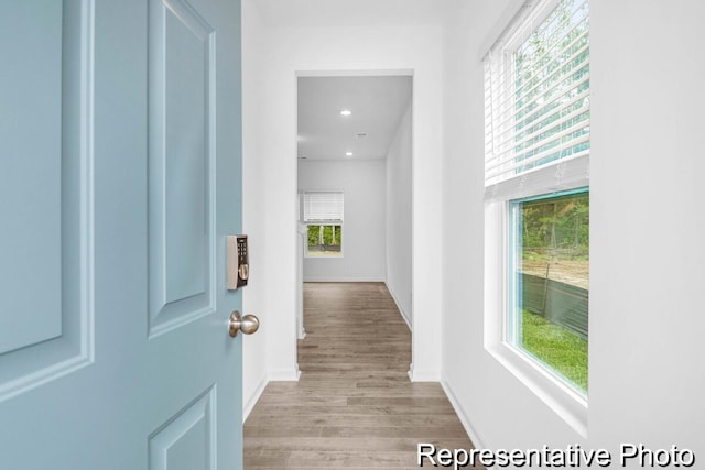 corridor with a wealth of natural light, light wood-type flooring, baseboards, and recessed lighting