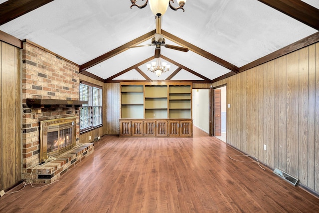 unfurnished living room with built in features, wooden walls, wood-type flooring, vaulted ceiling with beams, and a brick fireplace