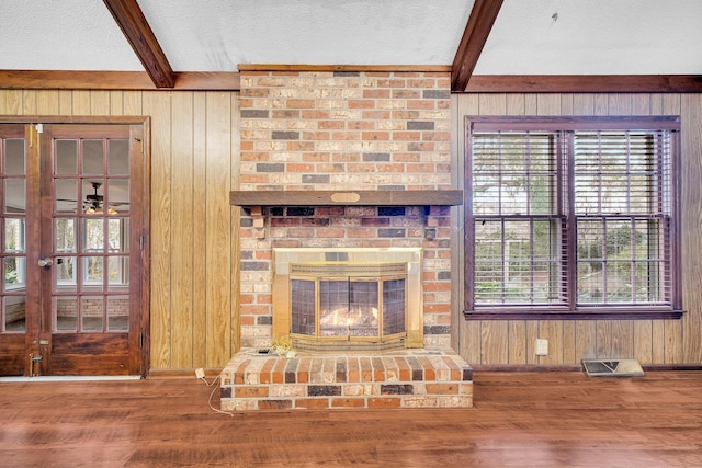 unfurnished living room with a brick fireplace, beam ceiling, wood-type flooring, and wood walls