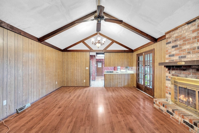 unfurnished living room with wood walls, hardwood / wood-style floors, a brick fireplace, and vaulted ceiling with beams