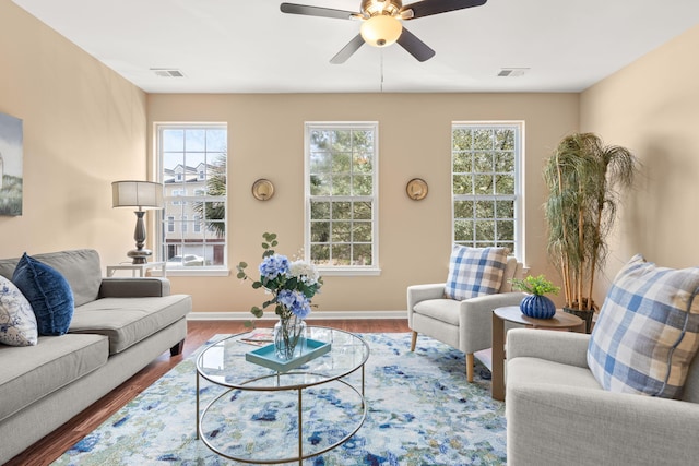 living area with a ceiling fan, visible vents, baseboards, and wood finished floors