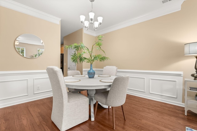 dining space with a wainscoted wall, visible vents, ornamental molding, wood finished floors, and a chandelier