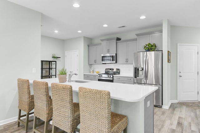 kitchen featuring a sink, stainless steel appliances, a kitchen bar, and gray cabinetry