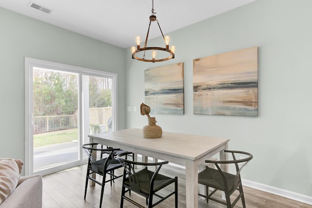 dining room featuring light wood finished floors, a notable chandelier, baseboards, and visible vents