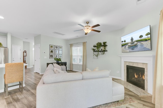 living room with light wood-style flooring, a ceiling fan, baseboards, and a premium fireplace